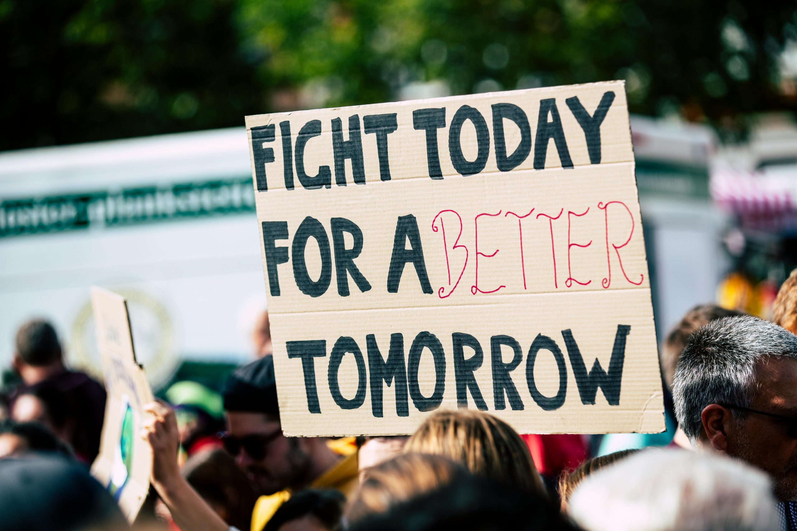 pexels-photo-2990644-2990644 Crowd holding a protest sign with 'Fight Today for a Better Tomorrow', outdoors and during the day.